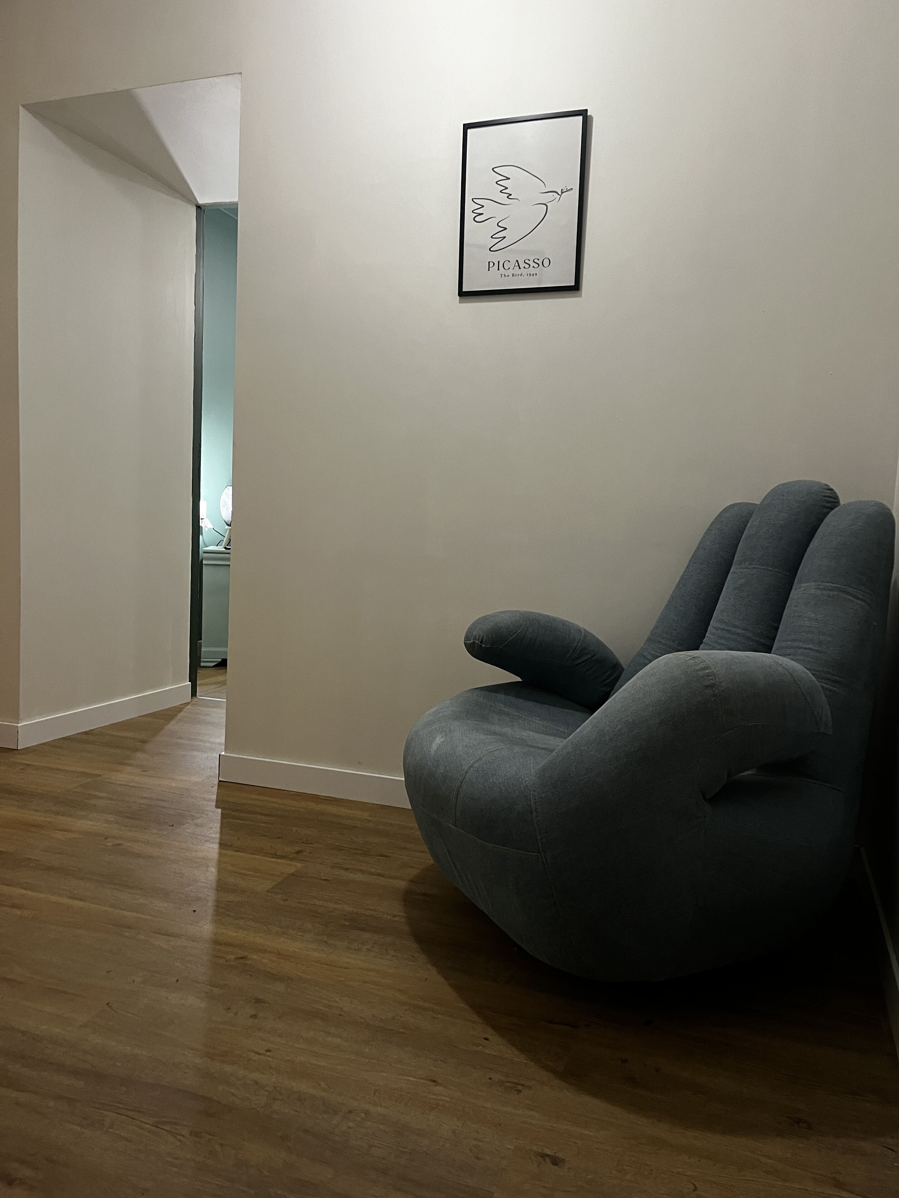 Une pièce avec un fauteuil en forme de poire de couleur grise, une œuvre d’art encadrée accrochée au mur et un plancher en bois.