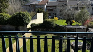 A balcony with a view of a stone house with a sloped roof, surrounded by greenery and hills. - Little paradise in Aveyron (Saint-Jean-du-Bruel)