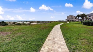 A paved pathway leading to a building with a beach view. - Pet Friendly | Ground Floor Sailmaker Villa | Covered Patio with Pool View (Fernandina Beach)