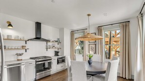 A modern kitchen with stainless steel appliances, a dining area with striped chairs, and a large window with curtains.