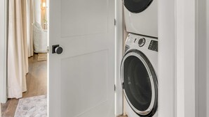 A laundry room with two stacked front-loading washers and dryers, a white door, and a wooden floor.
