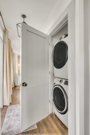 Un cuarto de lavado con dos lavadoras y secadoras de carga frontal apiladas, una puerta blanca y piso de madera.