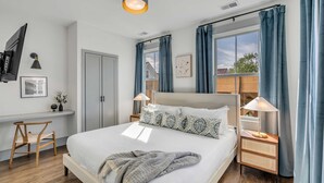 A modern bedroom with a large bed, bedside lamps, a TV, and a window with curtains.