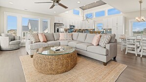A spacious living room with a large sectional sofa, a glass coffee table, and a ceiling fan.
