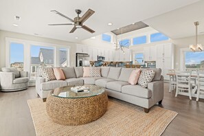 A spacious living room with a large sectional sofa, a glass coffee table, and a ceiling fan.
