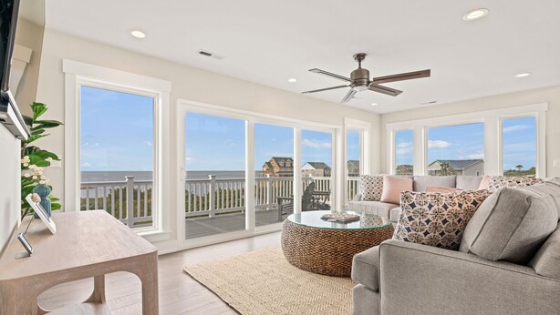 A spacious living room with a large window, a ceiling fan, and a view of the ocean.