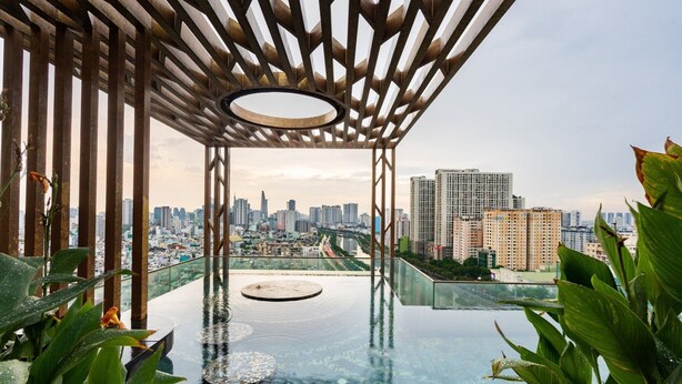 A rooftop infinity pool with a city view, surrounded by greenery and a wooden pergola structure.