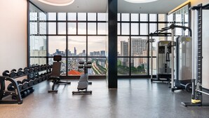 A gym with a city view, weight machines, dumbbells, and a bench.