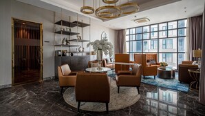 A modern hotel lobby with a marble floor, leather seating, a central round table, and a large window with a view of the city.
