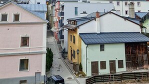 Rua residencial com casas coloridas, um carro estacionado e montanhas ao fundo.