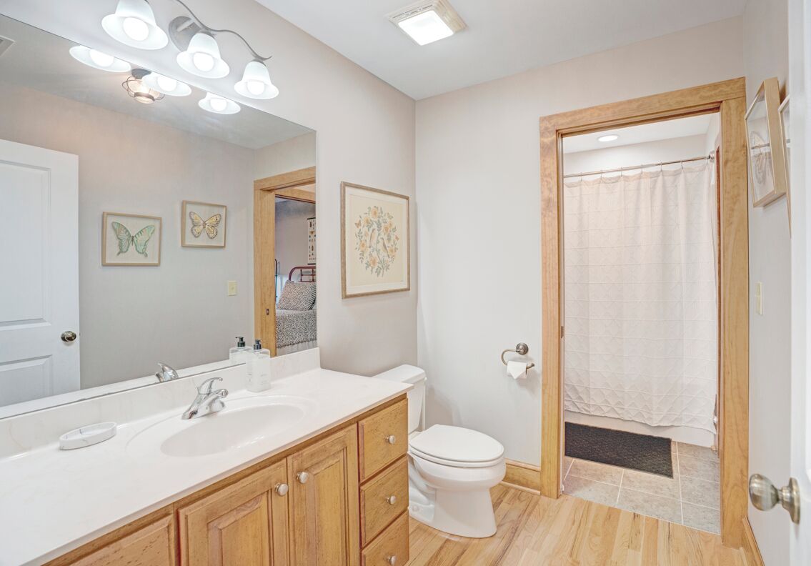 A bathroom with a white sink, wooden vanity, a white toilet, and a shower with a beige curtain.