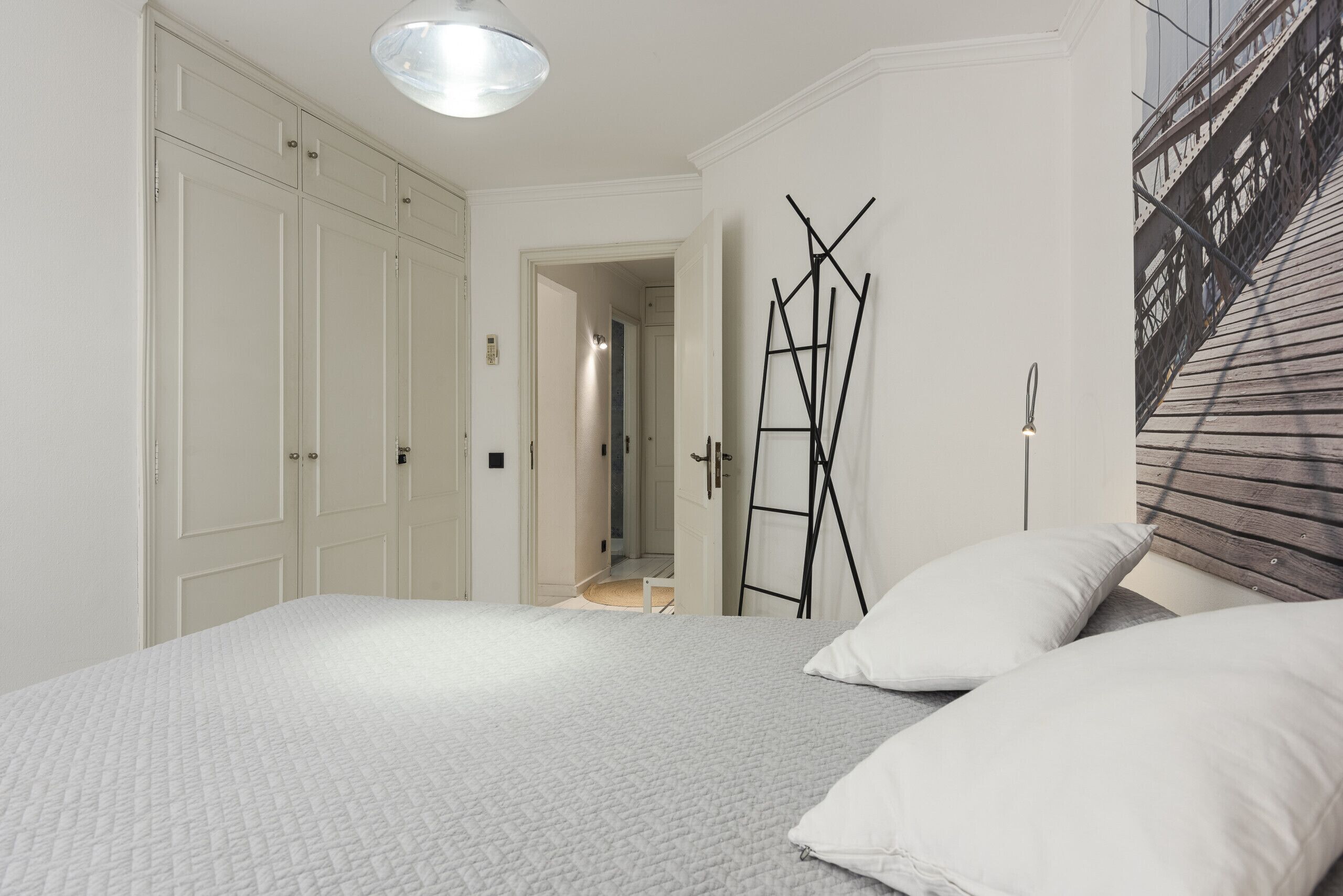 A bedroom with a bed, white walls, a wardrobe, and a ladder leaning against the wall.
