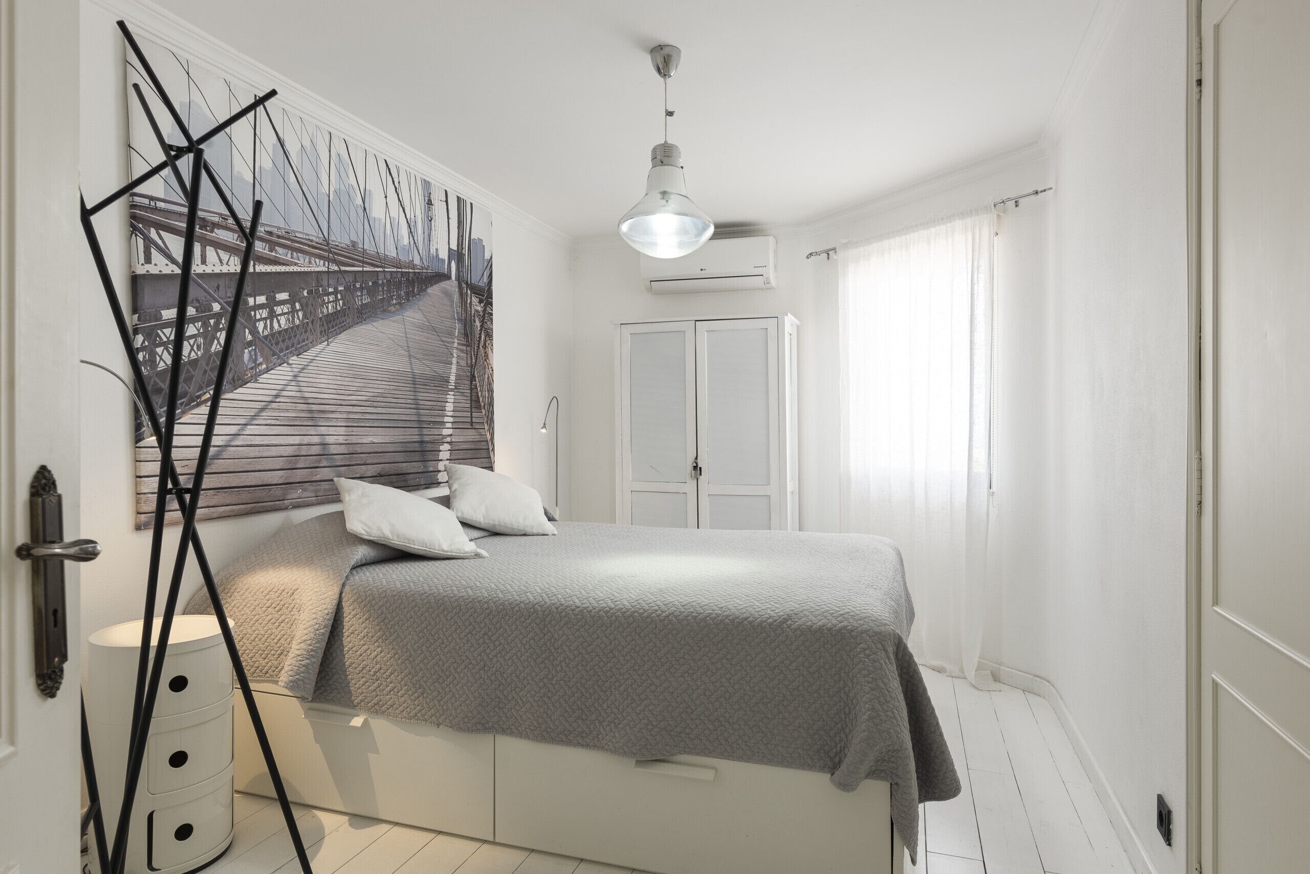 Ein Schlafzimmer mit Bett, Nachttisch, Wandlampe, Fenster mit Vorhängen und einer Tür.
