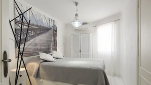 A bedroom with a bed, a nightstand, a wall-mounted lamp, a window with curtains, and a door. - Scandic - City Center by HD Properties (Vilamoura)