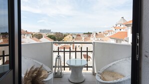 A balcony with a round table and wicker chairs, overlooking a cityscape with red-roofed buildings and a distant high-rise. - Scandic - City Center by HD Properties (Vilamoura)