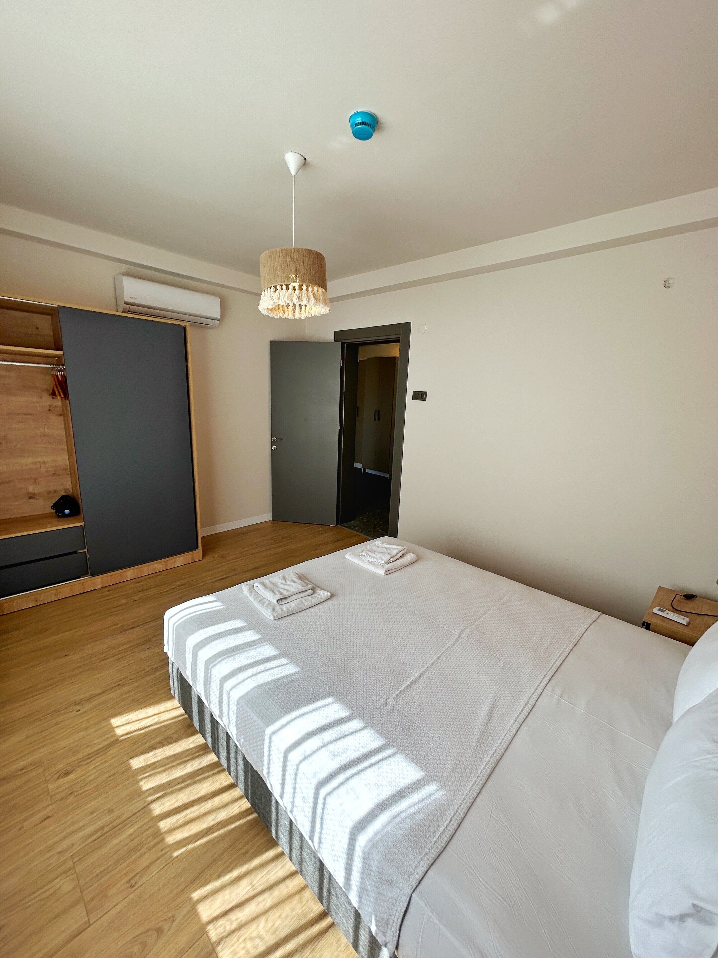 Una habitación de hotel moderna con una cama grande, un armario, un equipo de aire acondicionado y una puerta que da a otra habitación.