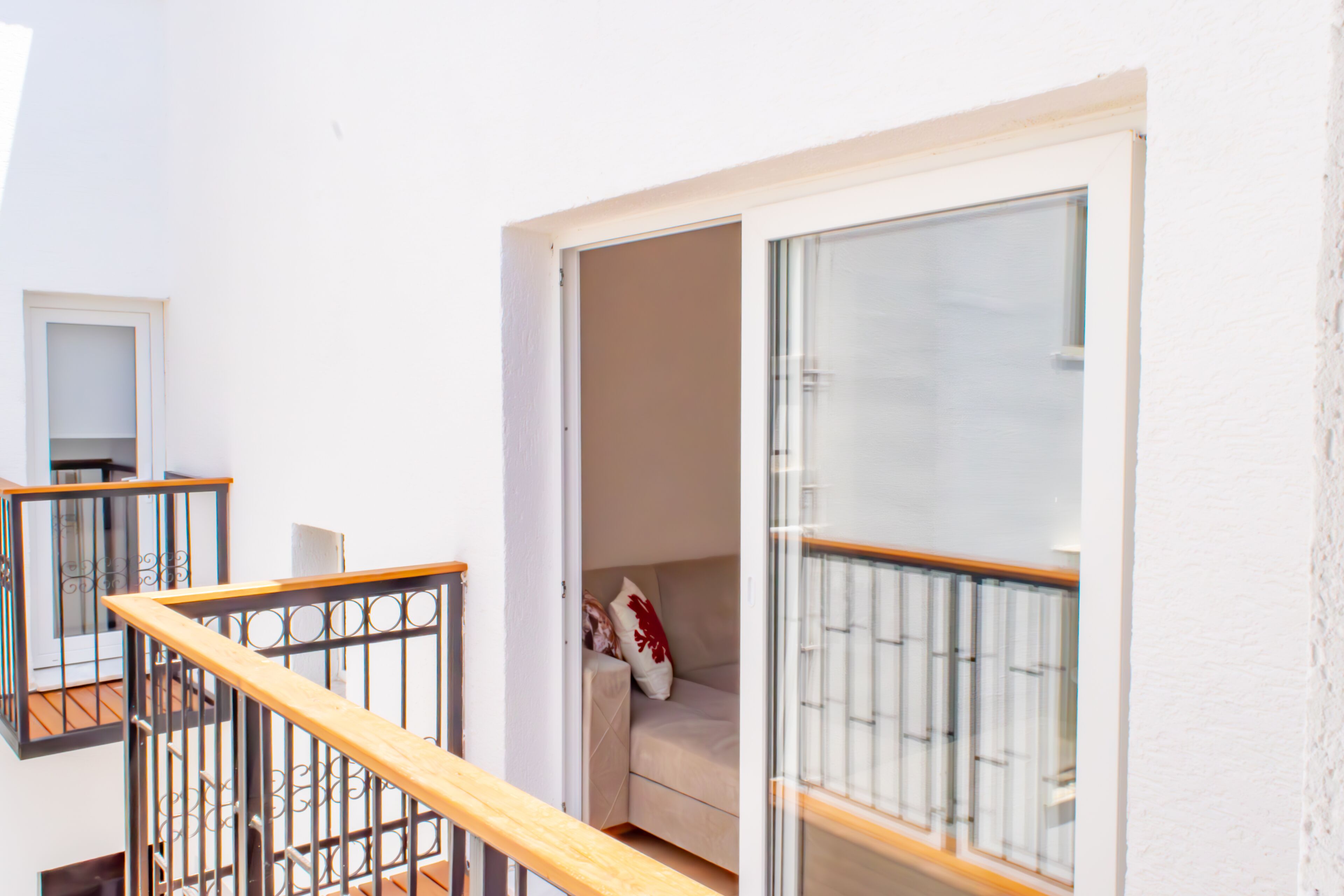 Una escalera con barandilla de madera que lleva a una habitación con puerta de vidrio y un sofá color crema.