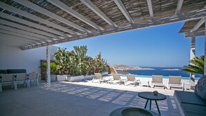 A covered outdoor seating area with a pool, lounge chairs, and a view of the sea. - Mykonos Town Villa (Mykonos)
