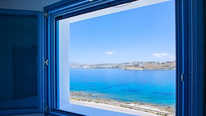 A room with a large window offering a view of a coastal landscape with a clear blue sea and distant hills. - Mykonos Town Villa (Mykonos)