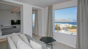 A modern room with a large window, a sofa, a small table, and a TV. - Mykonos Town Villa (Mykonos)