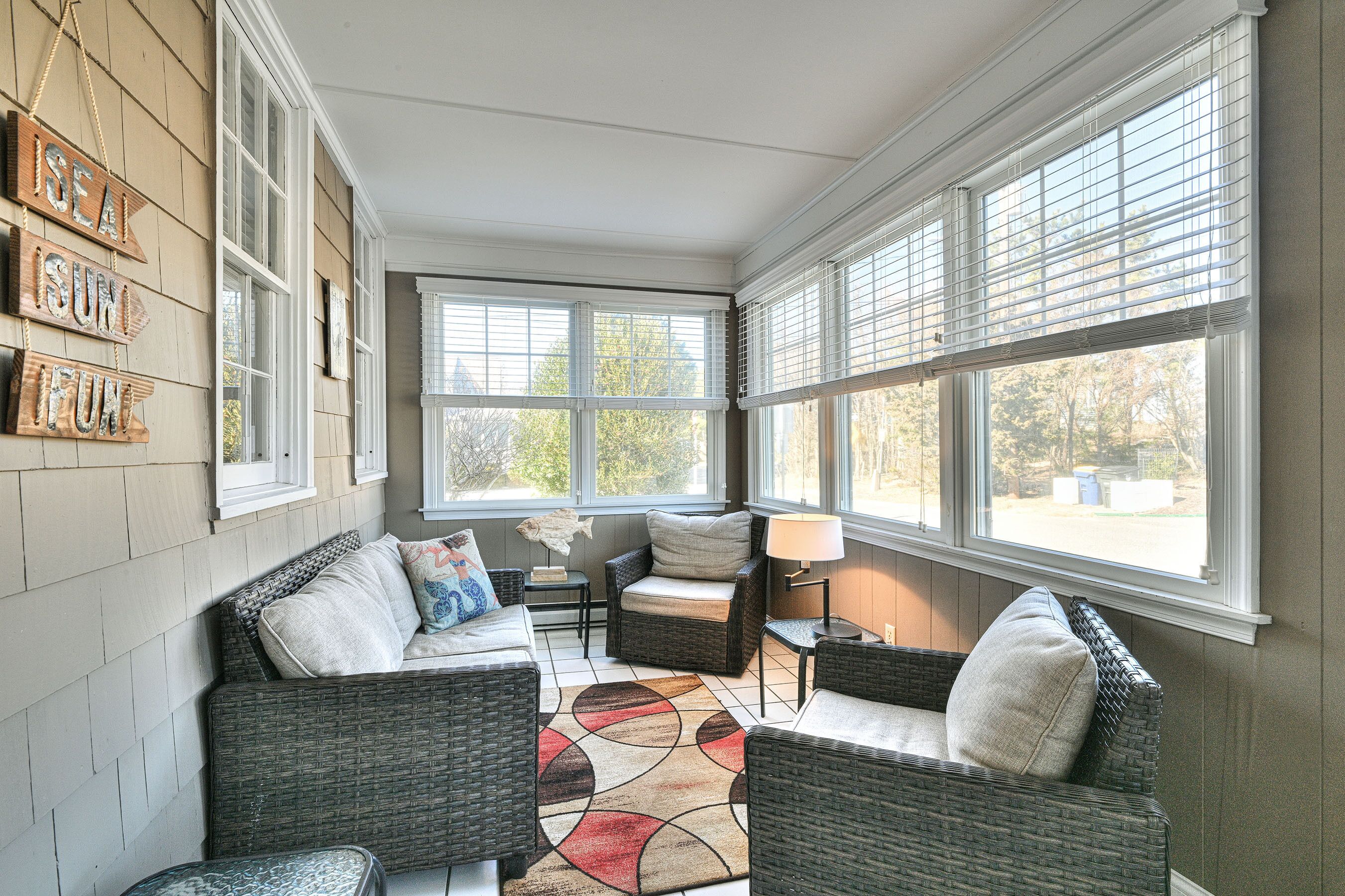 A sunroom with wicker furniture, a patterned rug, and a wall with 'SEA IS FUN' signs.