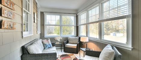 A sunroom with wicker furniture, a patterned rug, and a wall with 'SEA IS FUN' signs.