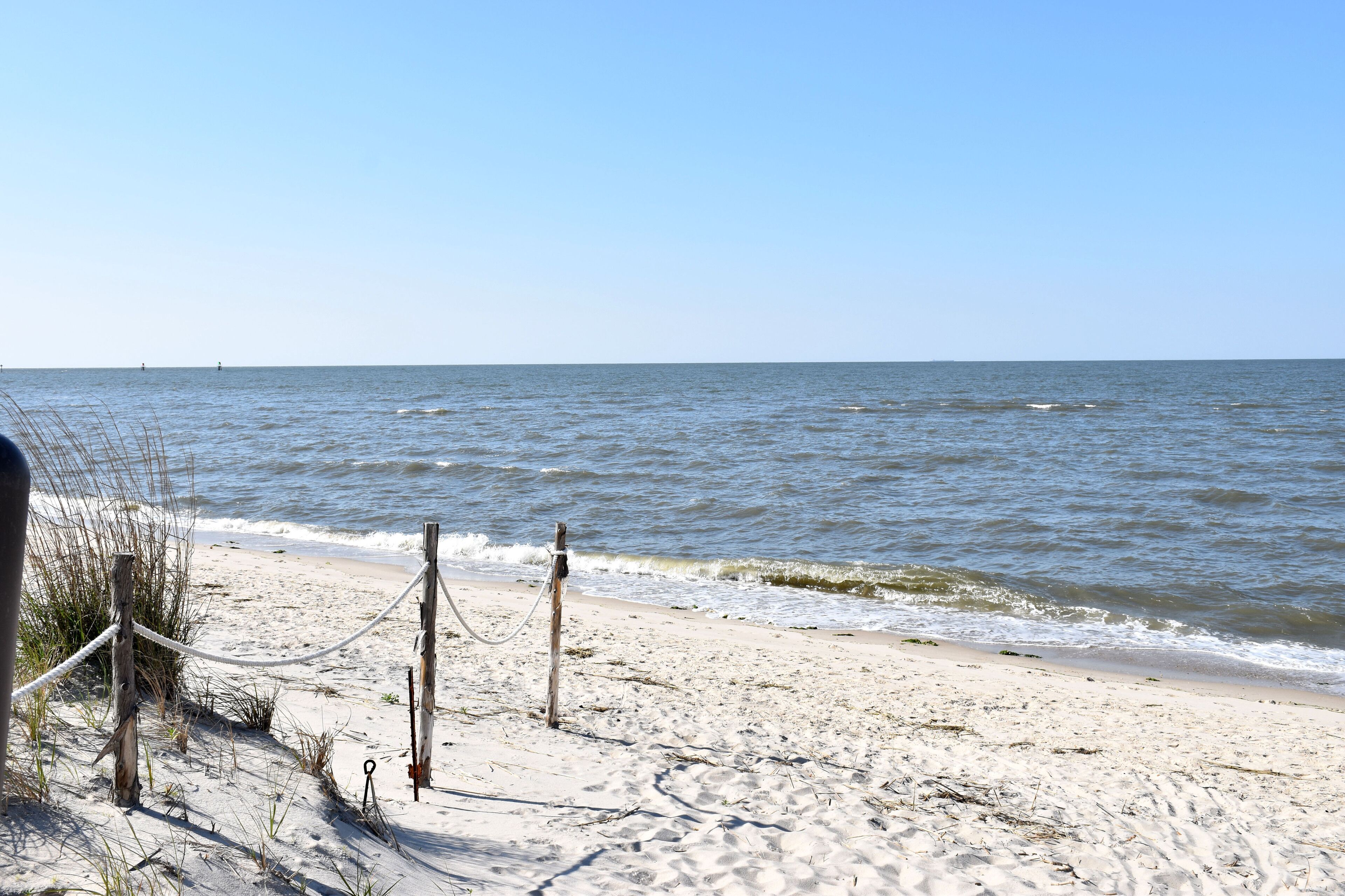 Une plage de sable bordée d’une barrière faite de cordes et de poteaux en bois.