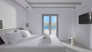 Een moderne hotelkamer met een groot bed, een flatscreen televisie aan de muur en uitzicht op de zee door een groot raam.