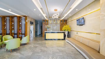 A modern reception area with a marble floor, a reception desk, a seating area, and a wall-mounted TV.