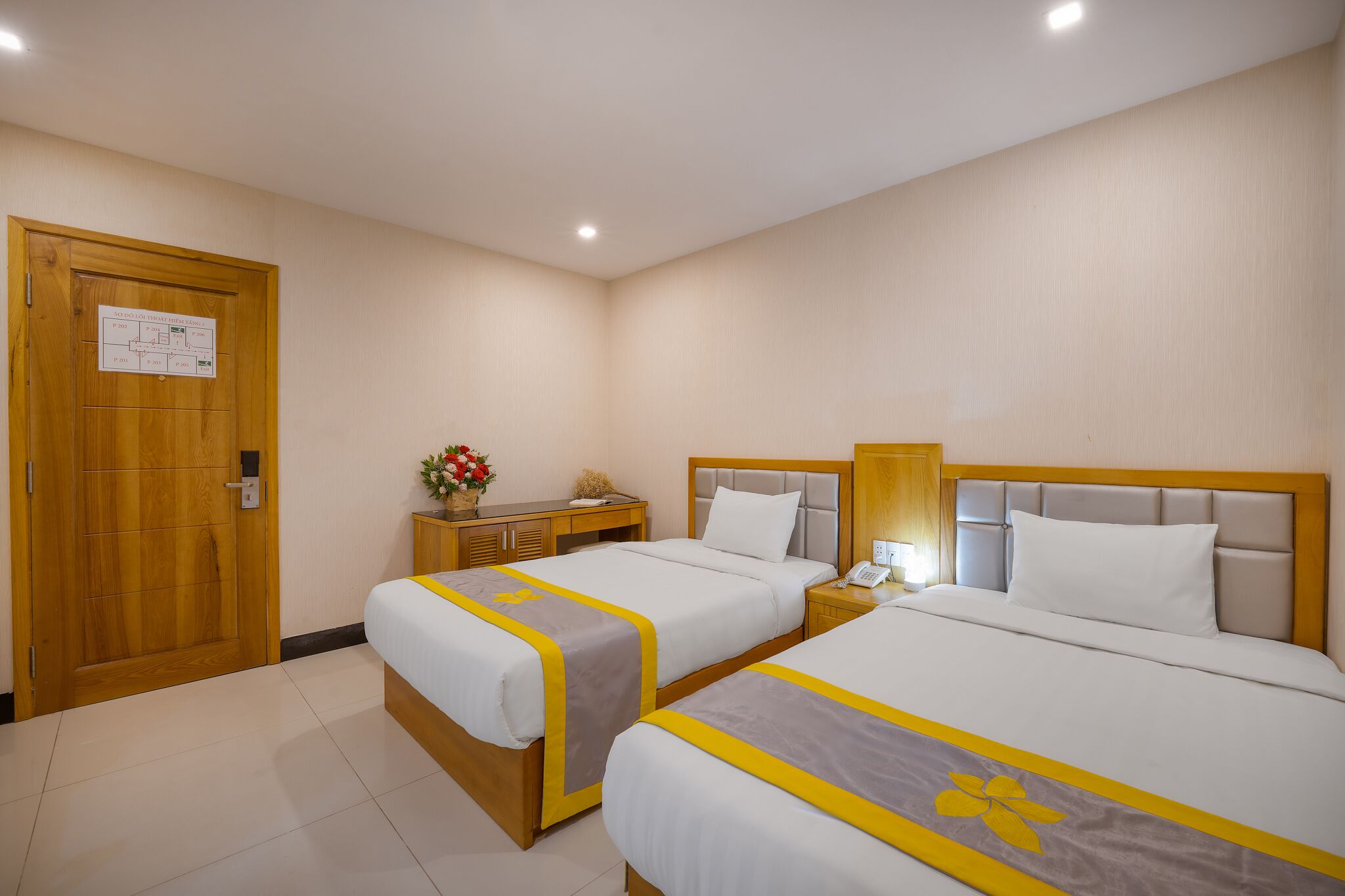 A hotel room with two beds, wooden headboards, a nightstand with a lamp, a wooden dresser, and a door with a sign.