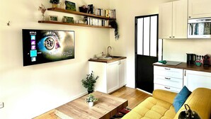 Un salon moderne avec un téléviseur à écran plat, une table basse en bois et un canapé jaune. On y trouve également un coin cuisine avec des meubles blancs et une porte à cadre noir.