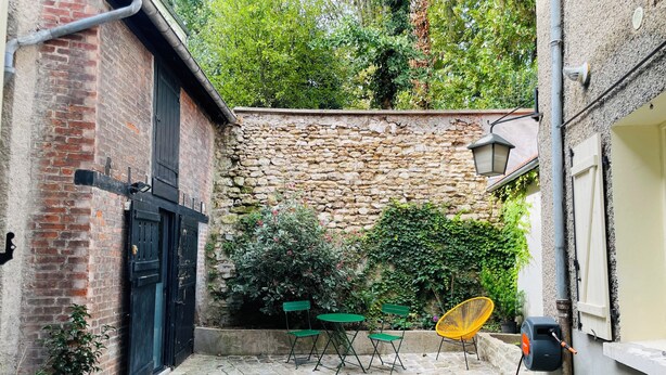 Une cour avec un sol en pierre, un bâtiment en briques, un mur en pierre et du mobilier d’extérieur.
