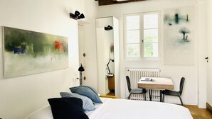 Une chambre à coucher avec un lit, un bureau et une chaise. Il y a une fenêtre qui donne sur un paysage verdoyant.