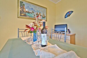 A dining table with a bottle of wine and two glasses, a vase with flowers, and a painting of a coastal scene on the wall. - One bedroom apartment, just few minutes from the beach - Lorena 2 (Umag)