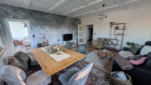 Una sala moderna con una mesa de comedor de madera, sillas tapizadas grises, un sofá negro y una alfombra roja con estampado.