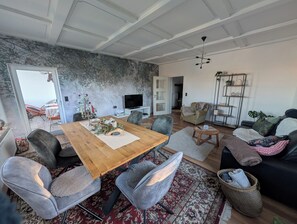Ett modernt vardagsrum med ett matbord i trä, grå klädda stolar, en svart soffa och en röd, mönstrad matta.