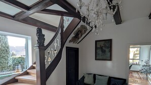Amplia sala de estar con escalera, un sofá verde oscuro y una araña.