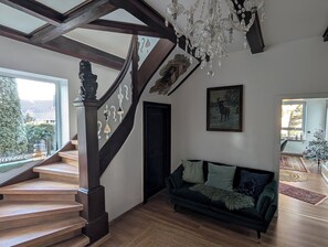 Ett rymligt vardagsrum med en trappa, en mörkgrön soffa och en kristallkrona.