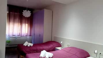 Camera da letto con due letti, un armadio, un termosifone e una finestra con tende.