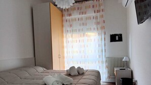 A bedroom with a bed, a radiator, a trash bin, and a window with curtains. - La Rosa dei Venti (Ortona)