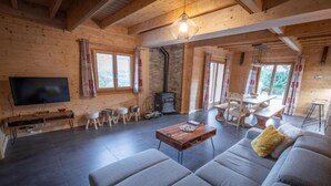Ein gemütliches Wohnzimmer mit großem Fernseher, Holzwänden, Kamin und Essbereich.