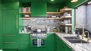 A green kitchen with a marble countertop, stainless steel appliances, and a gold faucet.