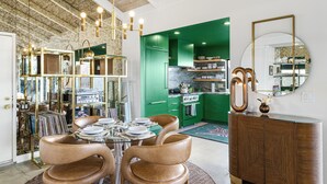 A dining area with a round table, leather chairs, and a glass-top table. There is a green kitchen in the background with green cabinets and a white countertop.