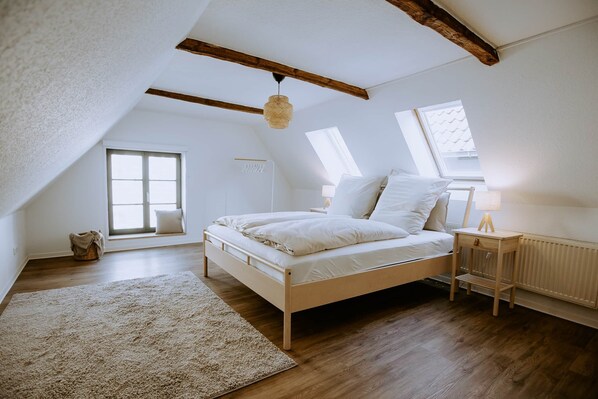 Een slaapkamer met een houten bed, een raam, een radiator en een plafond met zichtbare balken.