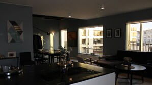 Een moderne woonkamer met een keuken, grote ramen en uitzicht op de stad.
