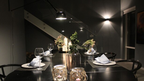 Een eettafel gedekt met kaarsen, glazen potten en wijnglazen, met een trap op de achtergrond.