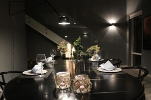 Una mesa de comedor dispuesta con velas, frascos de vidrio y copas de vino, con una escalera al fondo.