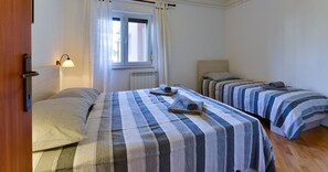 Una habitación con dos camas, una ventana con cortinas, una lámpara de pared y un radiador.