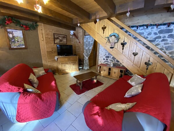 Una habitación acogedora con pared de piedra, vigas de madera en el techo, un televisor y sofás tapizados en rojo.