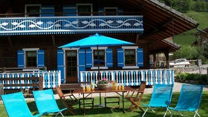 Un chalet de madera con balcón, una mesa con sillas y una sombrilla azul.